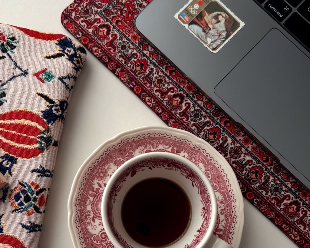 A cup of coffee, a computer and a fabric pencil case on a table.
