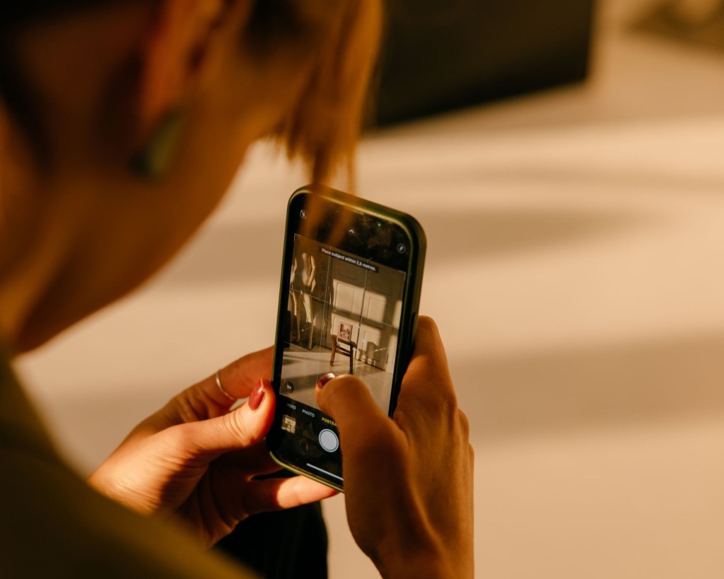 A person bending over a mobile phone taking a picture.